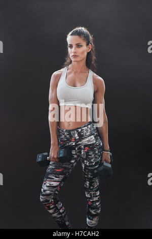 Vertikale Schuss der muskulöse junge Frau in Sportkleidung holding mit Gewichten und wegsehen. Frauen Fitness-Frau mit Hanteln o Stockfoto