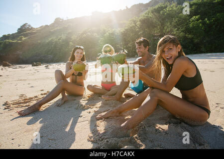 Gruppe junger Freunde Sommerurlaub am Strand mit frischen Kokosnuss Drink zu genießen. Junger Mann und Frauen Toasten mit Kokosnüssen auf Stockfoto