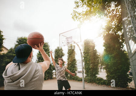 Streetball Spieler auf Platz Basketball zu spielen. Junger Kerl nehmen erschossen in den Korb mit Freund blockieren. Stockfoto