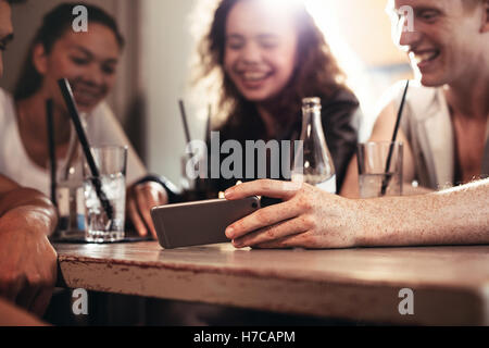 Gruppe von Freunden in einer Bar sitzen und beobachten ein lustiges Video auf Handy, Handy in der Hand des Menschen im Mittelpunkt. Stockfoto