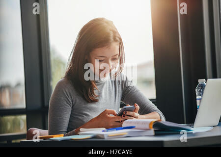 Schuss an glückliche junge Studentin am Tisch SMS auf ihrem Handy lesen. Asiatin mit Handy am col Stockfoto