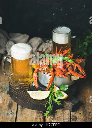 Zwei Pints Weißbier und gekochte Krebse mit Zitrone und Petersilie auf dunklen runden dienen Board über rustikalen hölzernen Hintergrund, se Stockfoto