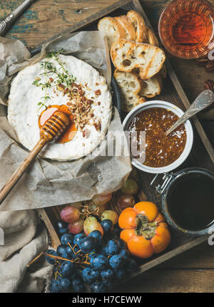 Käse, Obst und Wein festgelegt. Camembert in kleine Pfanne mit Nüssen und Kräutern, Trauben, Kaki, Feigenmarmelade, Honig, Baguette Scheiben und g Stockfoto