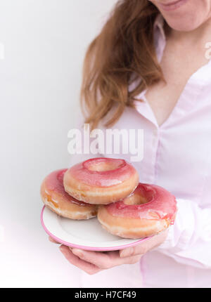 Eine Frau hält einen Teller mit rosa glasierte donuts Stockfoto