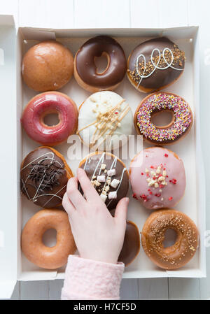 Eine Hand, eine Schachtel mit ein Dutzend Donuts einen Donut auswählen. Stockfoto