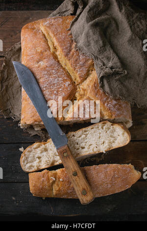 Frische handwerkliche Brot unter Sackleinen mit Vintage Messer über alten hölzernen Hintergrund. Draufsicht. Stockfoto