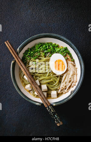 Asiatische Suppe mit grünem Tee Soba-Nudeln, Ei, Champignons, Frühlingszwiebeln und Tofu-Käse, serviert mit hölzernen Stäbchen Stockfoto