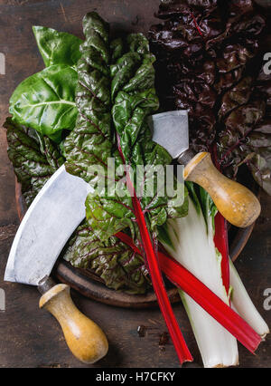 Vielzahl von frischen Mangold Mangold Salat Blätter auf Woode Schneidebrett mit Vintage Messer über alten dunklen hölzernen Hintergrund. Ansicht von oben Stockfoto