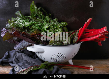 Frischen Mangold Salatblätter Mangold in weißen Sieb auf grauem Leinen-Serviette über alten dunklen hölzernen Hintergrund. Gesunde Ernährung Thema. Stockfoto