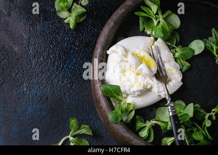 In Scheiben geschnitten italienischer Käse Burrata mit Olivenöl, frischen Feldsalat und Vintage Gabel in Ton Fach über strukturelle dunkel. Über Stockfoto