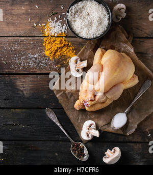 Ganze rohe Mini Huhn auf Backpapier mit Würze in Vintage Löffel, in Scheiben geschnittene Champignons und Schüssel mit ungekochtem Reis über o Stockfoto