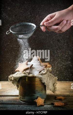 Hausgemachte Butterkekse Sternform sugar Cookies unterschiedlicher Größe in alten Blechdose Sackleinen Lappen mit Sieb bestreuen Zuckerpulver aus Stockfoto