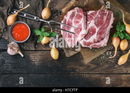 Rohes Steak Fleisch Schweinekamm auf gebackene Papier mit Schalotte Zwiebel, Tomate Soße Marinade, Basilikum und Gewürzen, serviert mit Fleisch Gabel ov Stockfoto