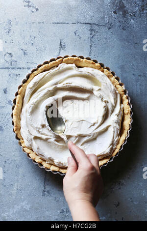 Hand mit der Rückseite eines Löffels zu verbreiten, die geschlagene Sahne auf dem Boden einer Torte füllen. Ansicht von oben Stockfoto