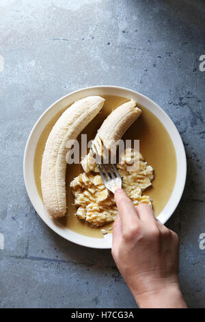 Weibliche Hand Maischen Banane mit einer Gabel einstechen. Ansicht von oben Stockfoto