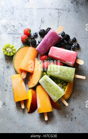 Eis am Stiel mit Kiwi, Mango, Melone, Heidelbeeren, Brombeeren und Erdbeeren über frisches Obst. Ansicht von oben Stockfoto