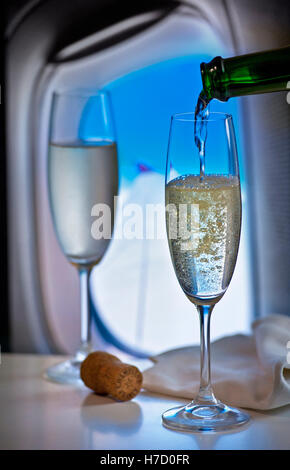 FIRST CLASS Luxus fliegen Gießen Champagner während des Fluges in Luxus-Kabine mit Fenster und Flugzeug Flügel hinter Stockfoto