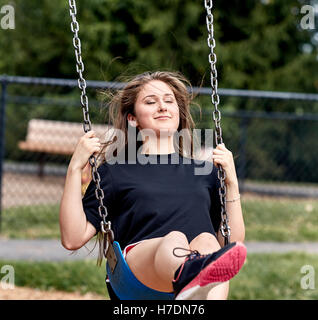 Junges Mädchen schwingen auf einer Schaukel auf einem Spielplatz mit geschlossenen Augen und Lächeln Stockfoto