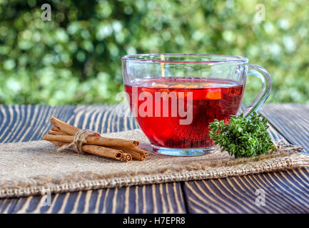 Tasse Tee mit verschiedenen Kräutern und getrockneten Früchten auf einem Holztisch im freien Stockfoto