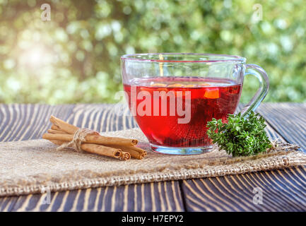 Tasse Tee mit verschiedenen Kräutern und getrockneten Früchten auf einem Holztisch im freien Stockfoto