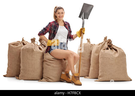 Bäuerin halten eine Schaufel und sitzen auf Sackleinen Säcke isoliert auf weißem Hintergrund Stockfoto