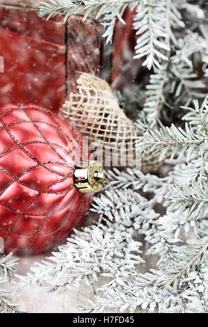 Rote Christbaumkugel von einer alten antiken Holzkiste mit Schnee bedeckten Kiefer Ästen um ihn herum. Extrem geringe Schärfentiefe Stockfoto
