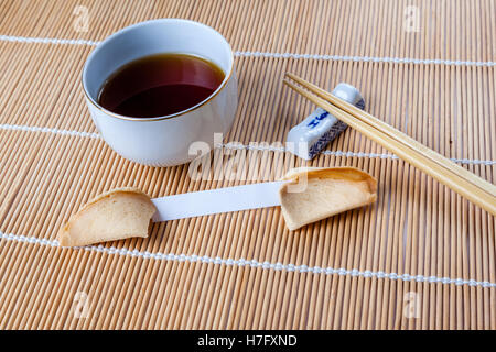 Chinesische Tasse Glückskeks mit leeren Slip auf Bambusmatte mit chinesischen Essstäbchen und Tee eingeritten. Stockfoto