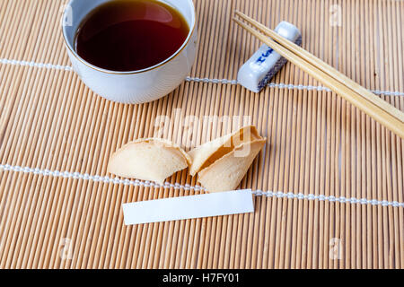 Chinesische Tasse Glückskeks mit leeren Slip auf Bambusmatte mit chinesischen Essstäbchen und Tee eingeritten. Stockfoto