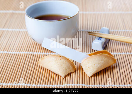 Chinesische Tasse Glückskeks mit leeren Slip auf Bambusmatte mit chinesischen Essstäbchen und Tee eingeritten. Stockfoto