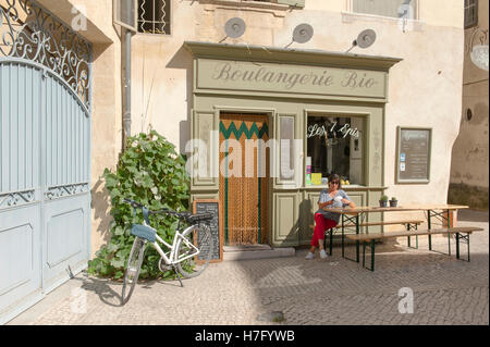 Weibliche Radfahrer (Claudia Albrecht) sitzen auf einer Bank vor einer Öko-Bäckerei in Tarascon, Provence, Frankreich Stockfoto