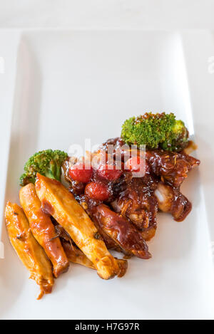 Schweinefleisch Rippe gegrillte und gebratene Kartoffelspalten auf weißen Teller mit Sauce und Gemüse, Gourmet-Küche. Stockfoto