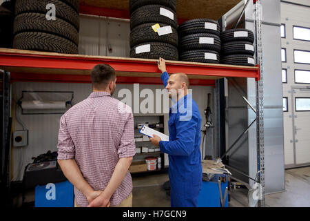 Kfz-Mechaniker und Mann mit Reifen bei Car shop Stockfoto