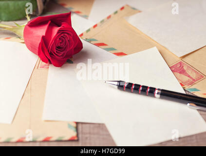 Vintage Umschläge, rote Rosen und Blätter verstreut auf dem Holztisch für romantische Briefe zu schreiben. Stockfoto