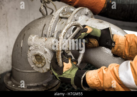 Mann in Schutzhandschuhen und Orange Overall ist öffnen/schließen Rohr Ventil Stockfoto