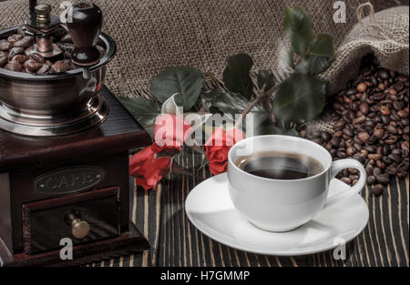 Kaffeemühle, rote Rose und Tasse Kaffee auf alten Schreibtisch aus Holz Stockfoto