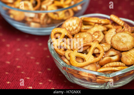 Mischung aus salzige Snacks (Kekse und Brezeln) in Glasschüssel auf rotem Grund Stockfoto