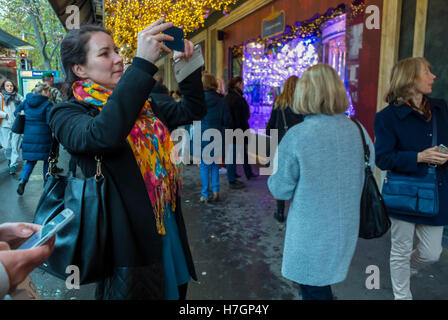 Paris, Frankreich, eine große Menschenmenge, die Weihnachtslichter genießt, Weihnachtsfenster einkauft, Le Printemps Kaufhaus, Frau, die Fotos mit dem Smartphone auf dem Bürgersteig macht Stockfoto