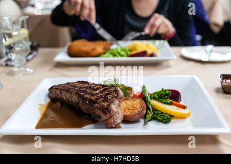 Ein köstliches Streifen Lende Rindfleisch Steak Essen serviert mit frischem Gemüse und Marsala Portobello Pilzsauce. Absichtliche flach de Stockfoto