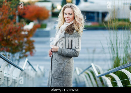 Schöne Blondine mit lockigem Haar stehend auf Treppen im Freien im Herbst Stockfoto