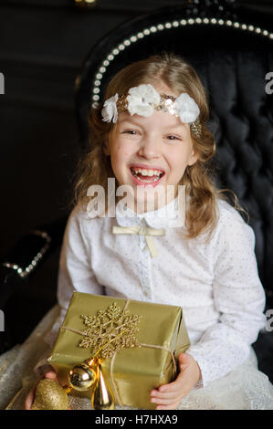Schöne Mädchen fotografierte für die Weihnachtskarte. Mädchen trägt einen weiß-Gold-Kleid mit einem Kranz auf dem Kopf. Sie sieht aus wie ein C Stockfoto