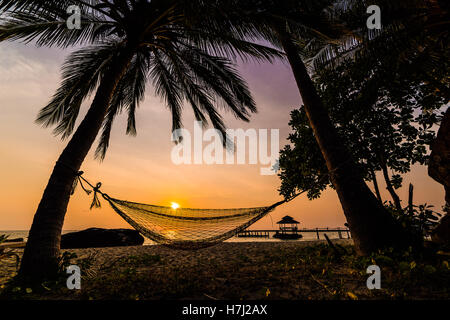 Tropisches Paradies: Sonnenuntergang am Meer - dunklen Silhouetten der Hängematte und Palmen Stockfoto