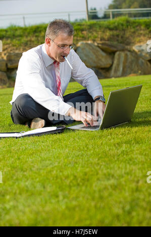 Geschäftsmann, sitzend in einem Park mit einem laptop Stockfoto
