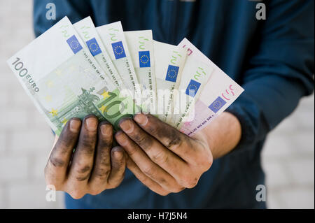 Symbolisches Bild von Schwarzgeld, manuelle Arbeiter mit schmutzigen Händen hält Banknoten Stockfoto