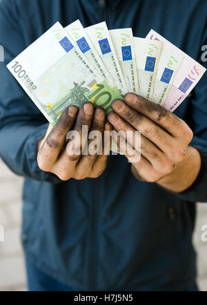 Symbolisches Bild von Schwarzgeld, manuelle Arbeiter mit schmutzigen Händen hält Banknoten Stockfoto