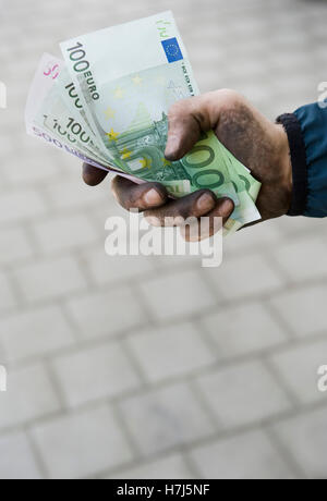 Symbolisches Bild von Schwarzgeld, manuelle Arbeiter mit schmutzigen Händen hält Banknoten Stockfoto