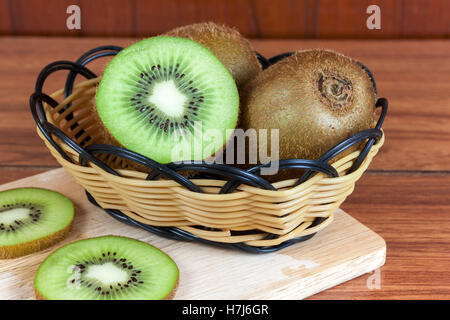 frische Kiwis und Scheiben von Kiwifrucht im Korb auf Holz Stockfoto