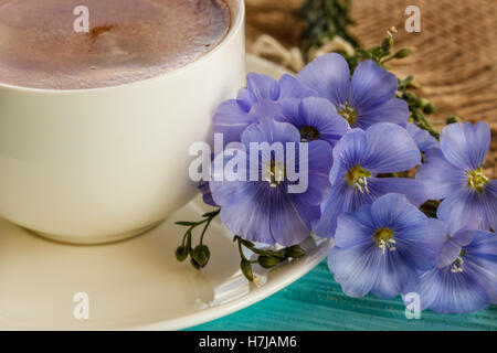 Kaffeebecher mit blauen Blüten und Notizen guten Morgen Frühstück am blauen rustikalen Tisch von oben, Stockfoto