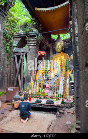 Ein kleiner Junge auf einem buddhistischen Schrein innen Wat Phu, eine ruinierte Khmer Hindu Tempelanlage in Champasak im Süden von Laos zu beten. Stockfoto