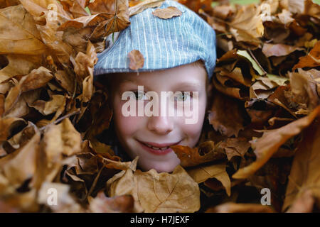 Happy Herbst. Junge im Retro-flache Kappe aus trockenen Blätter Haufen im Herbst Park suchen. Stockfoto