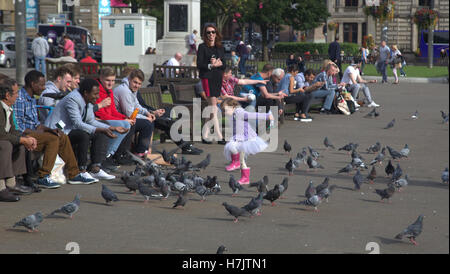 Touristen und Einheimische genießen kleine Mädchen spielen mit Tauben in George square Stockfoto